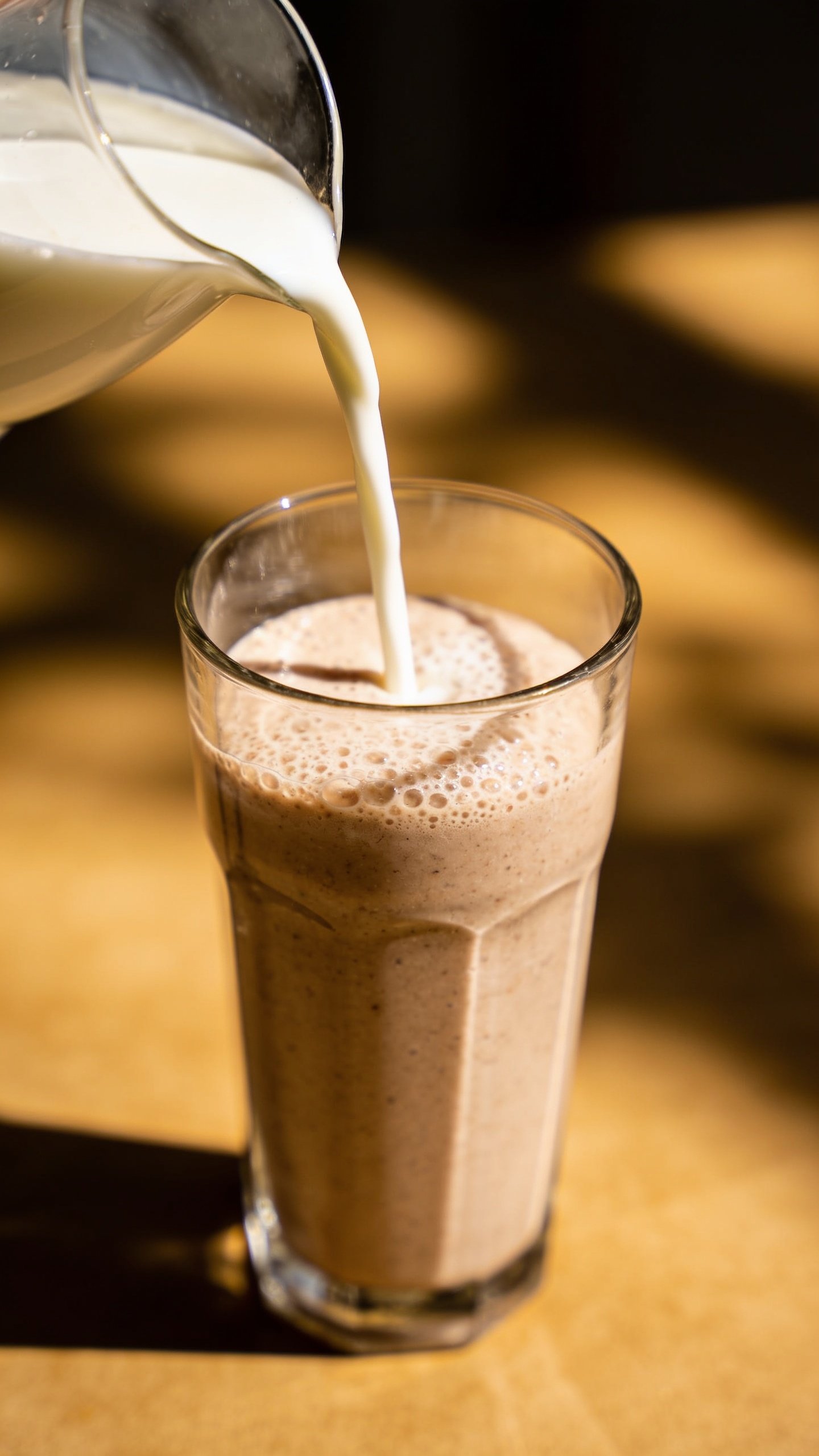 Closeup of milk being poured into a smoothie in a tall glass, soft focus background