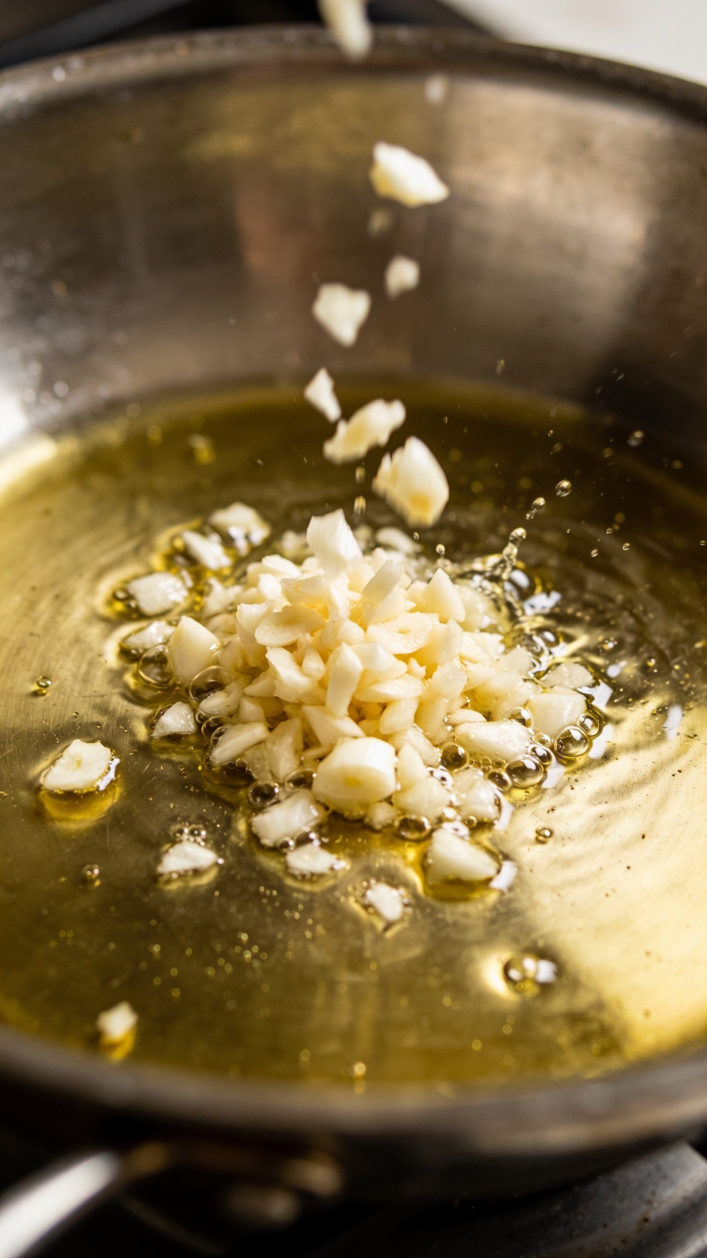 closeup of minced garlic hitting hot olive oil in skillet
