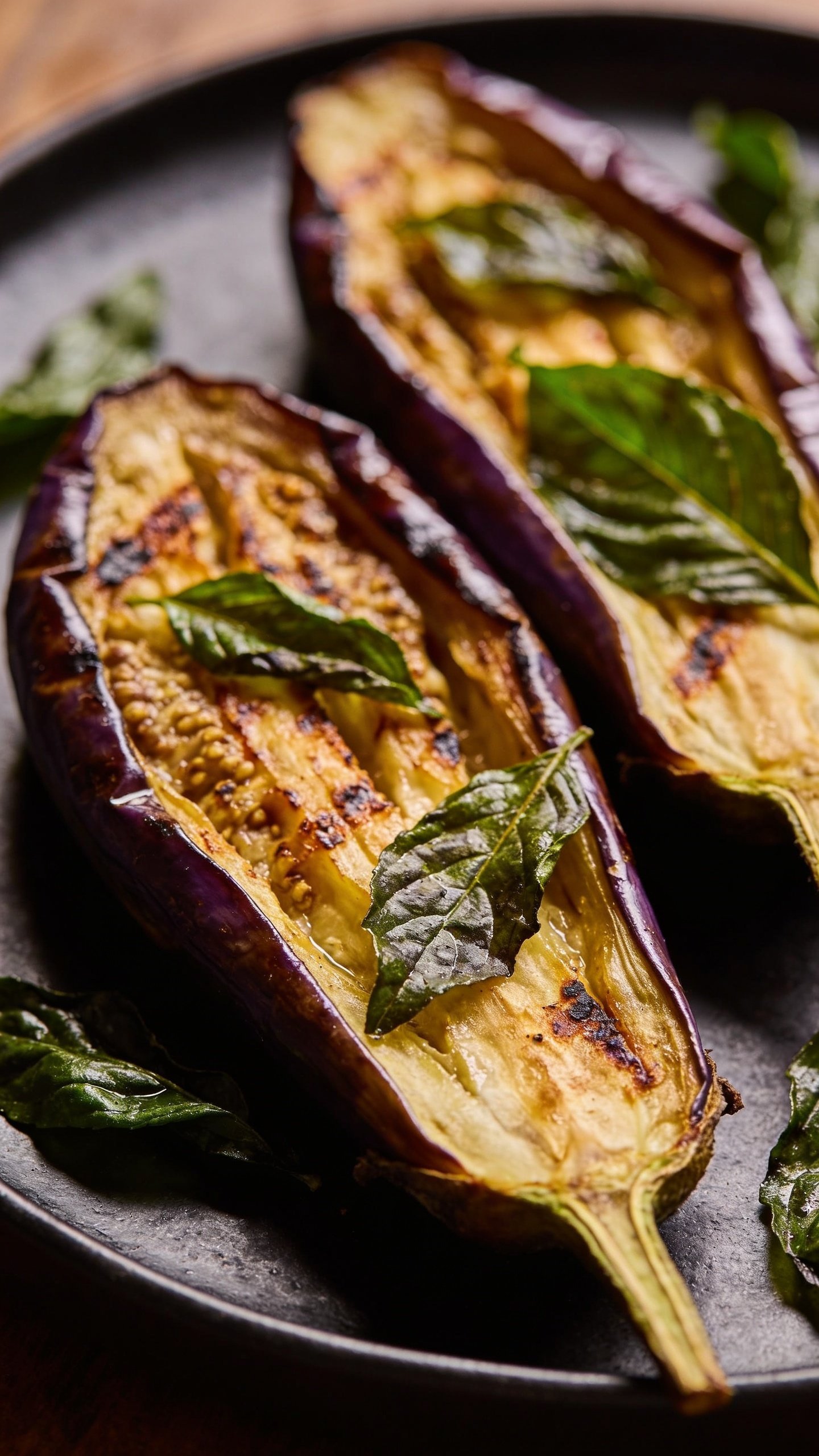 closeup of roasted Thai basil eggplant halves on a dark plate