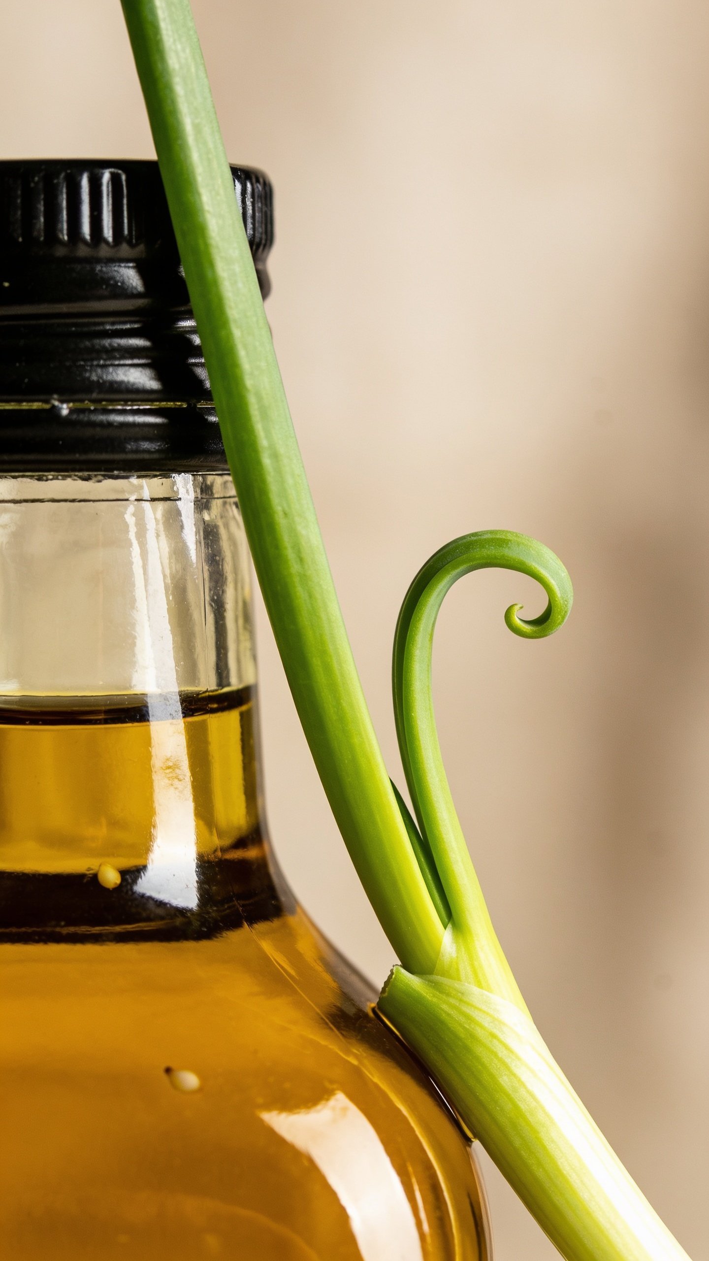 Closeup of a single green onion strand curling over a glossy sesame oil bottle