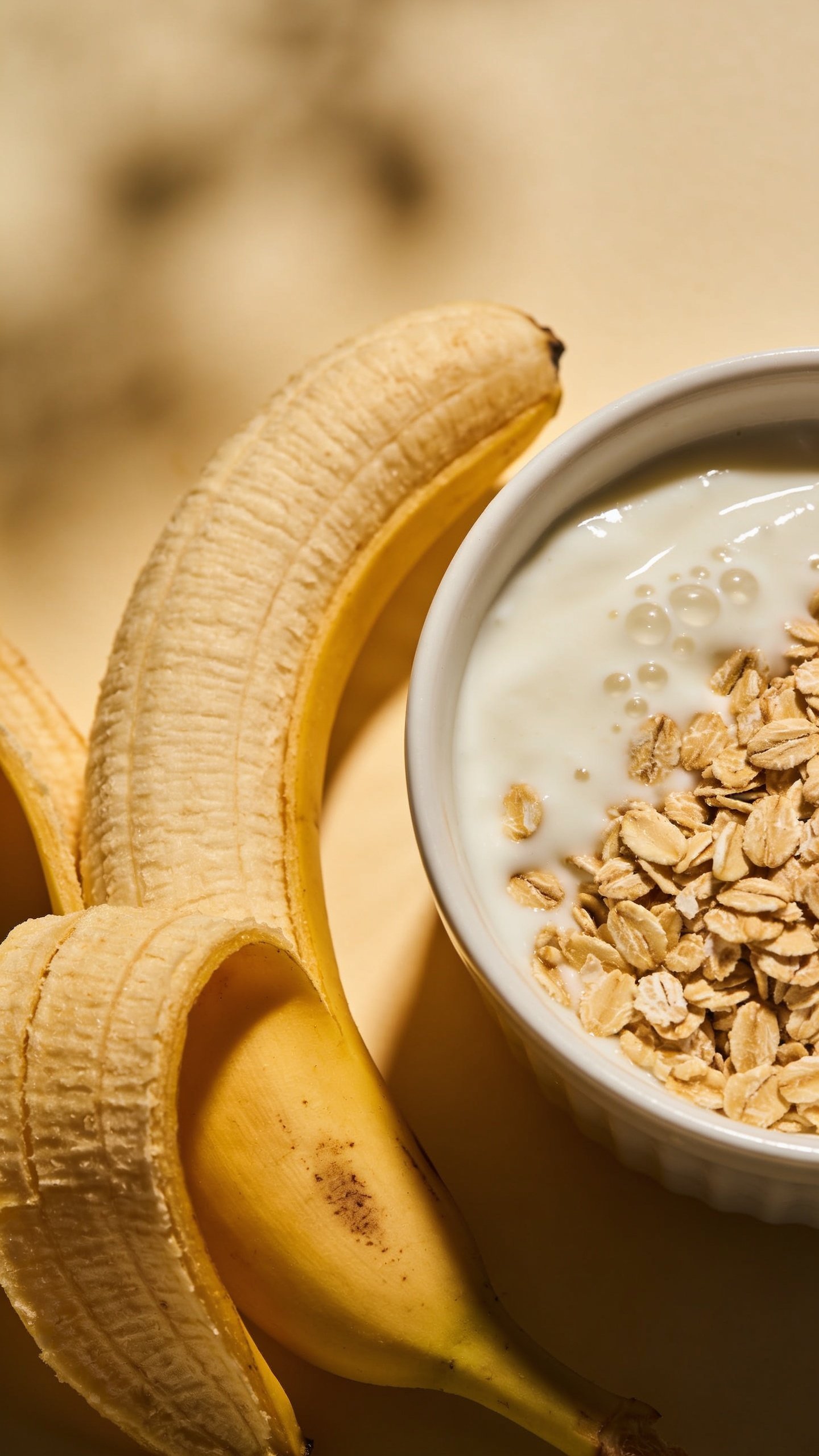 closeup of a single ripe banana beside a bowl of oats and yogurt