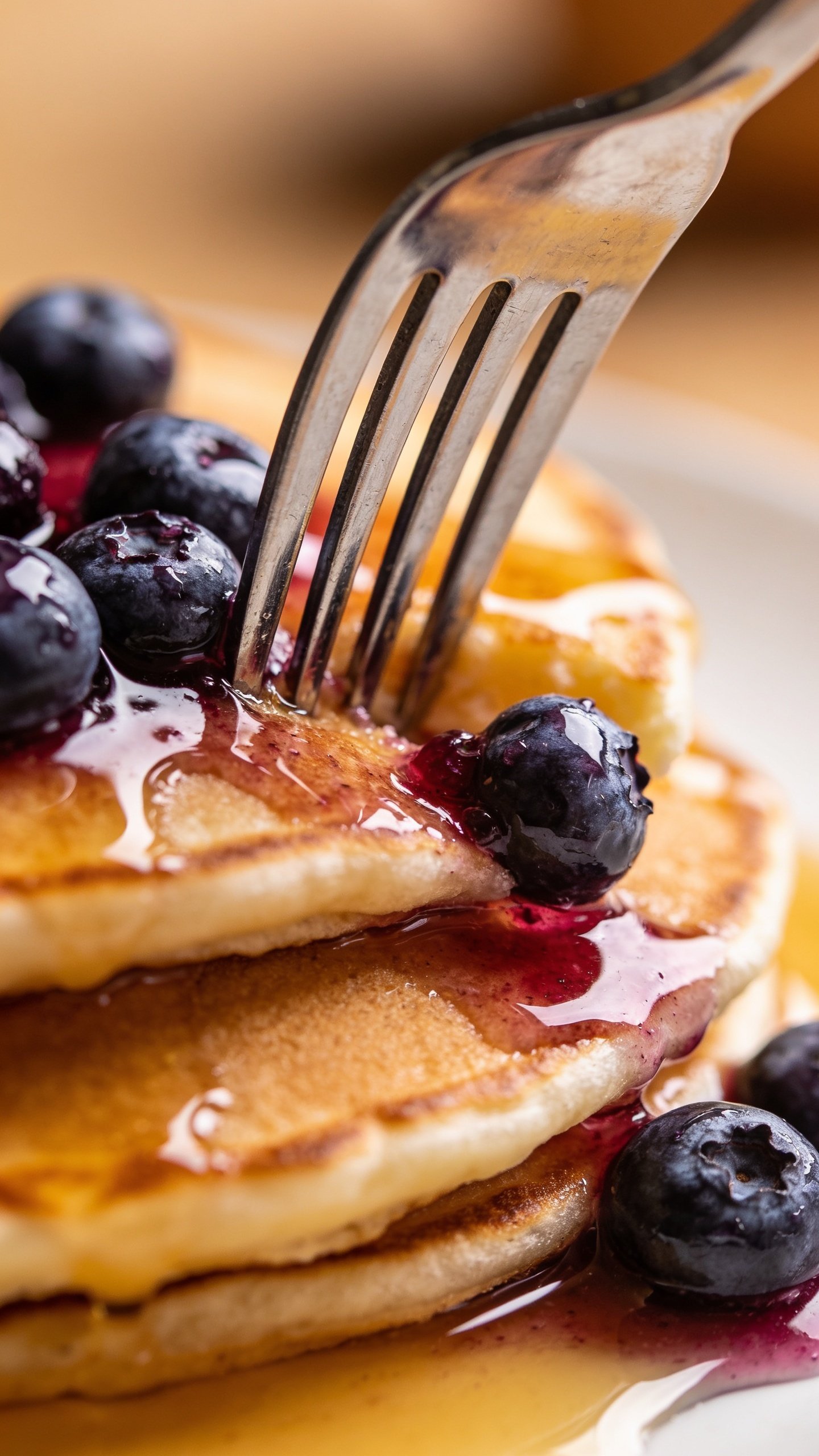 Close-up of fork piercing a pancake with blueberry bursting smeared glaze