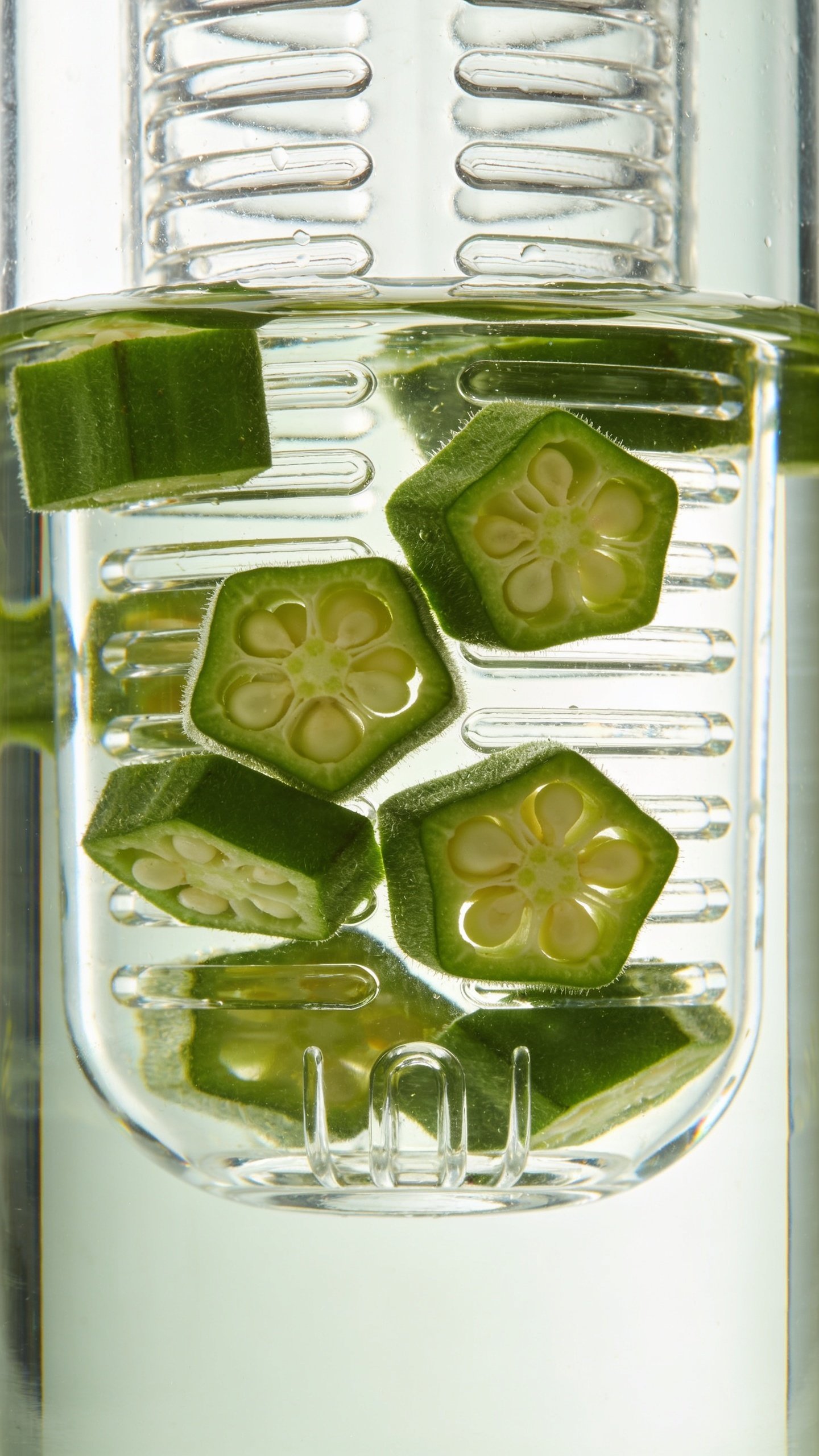 Closeup of a single glass infuser bottle with okra slices and water