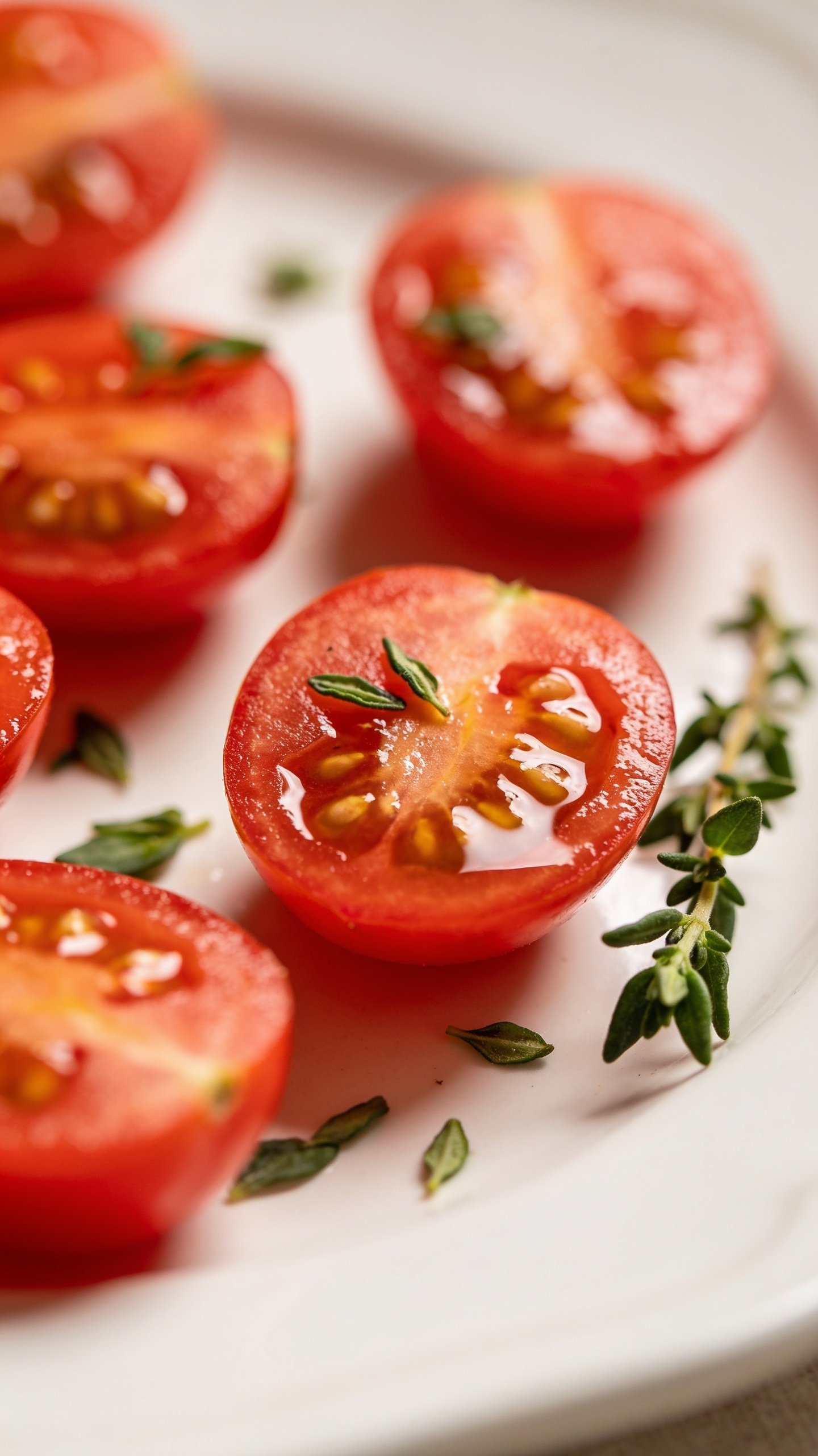 Closeup of halved cherry tomatoes on a white plate, herb sprig garnish